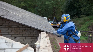 Two men in hazard suits removing asbestos sheets from a roof